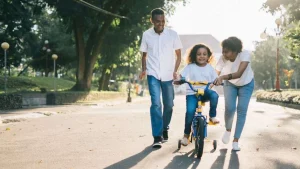 Dad, mom, and daughter are enjoying an afternoon together, teaching her to ride a bicycle. A way of surrendering to love.